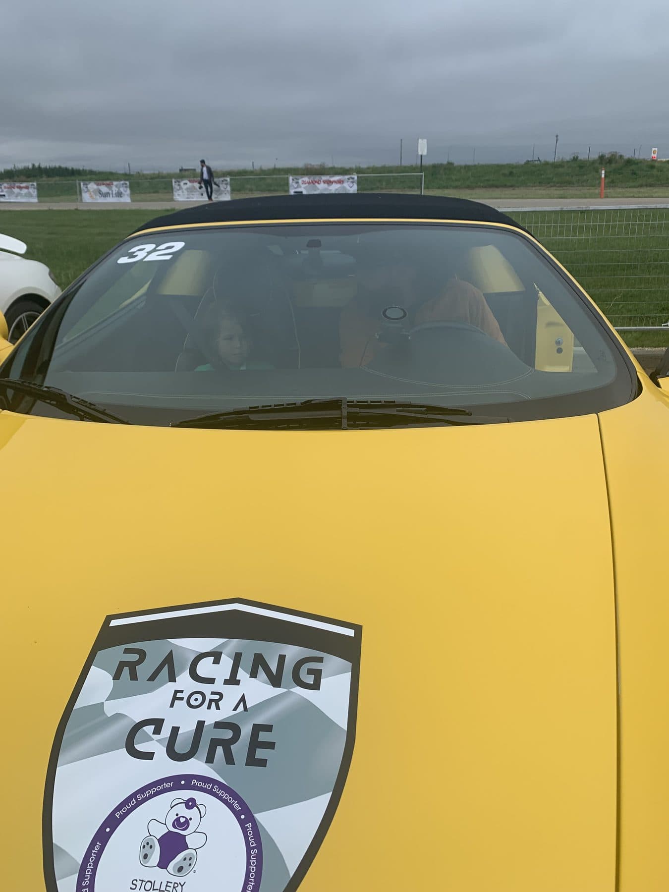 The Racing for a Cure shield decal on the hood of a yellow Ferrari at a charity racing event.